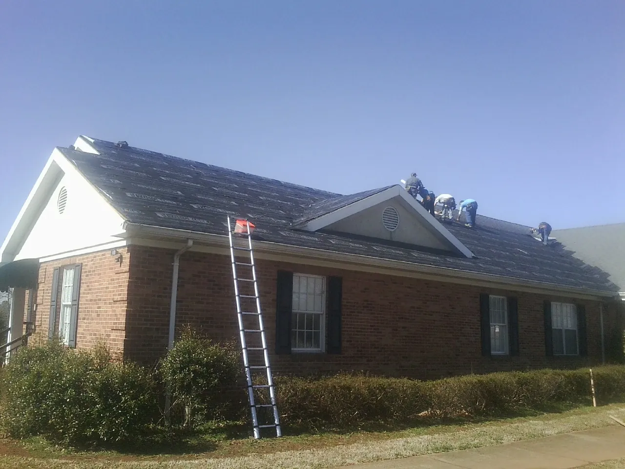 Crew tearing shingles off a brick ranch roof with a ladder set — Metal Roof Repair work by our crew in Henderson