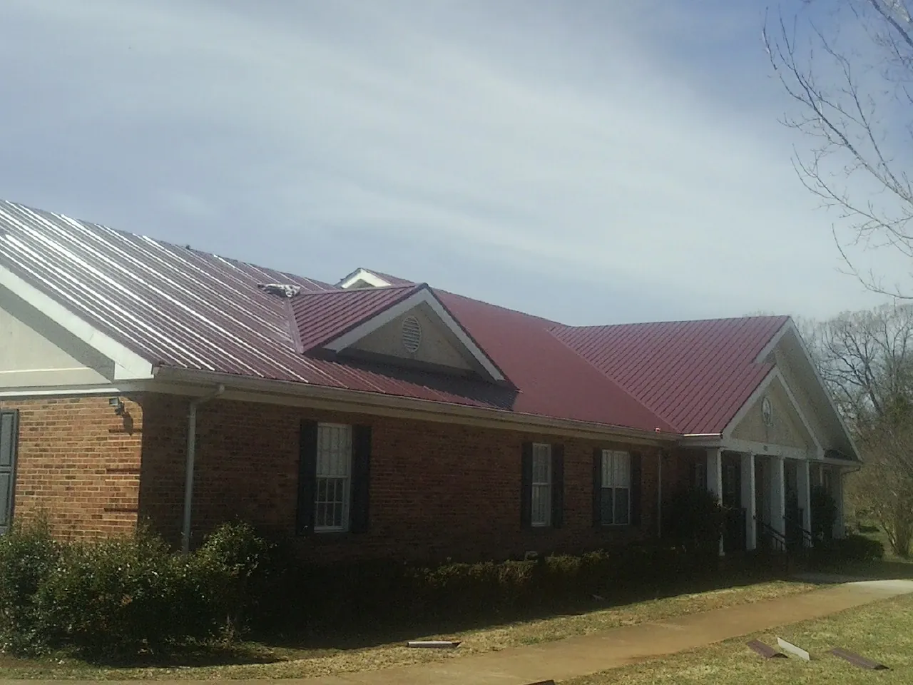 Red metal roof with gabled entries on a long brick building, from a Hail Damage Roof Repair job in Henderson