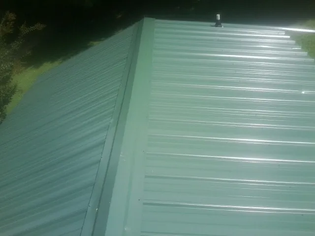 New green metal panels meeting at the ridge of a roof — Flat Roof Repair work by our crew in Henderson